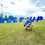 Andrew Boungnavong crouching in front of bolt up sign